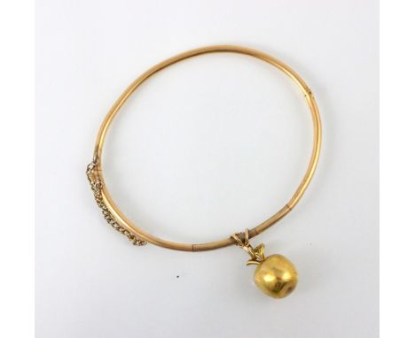 A yellow metal bangle, the hollow bangle, unmarked, suspending an associated charm designed as an apple, stamped with 9ct imp