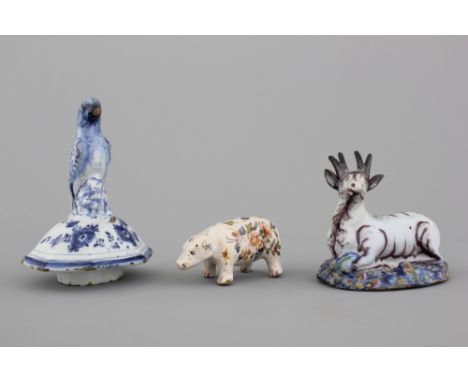 A Dutch Delft polychrome model of a seated deer 18th C. Together with a blue and white parrot-finial lid and a French faience