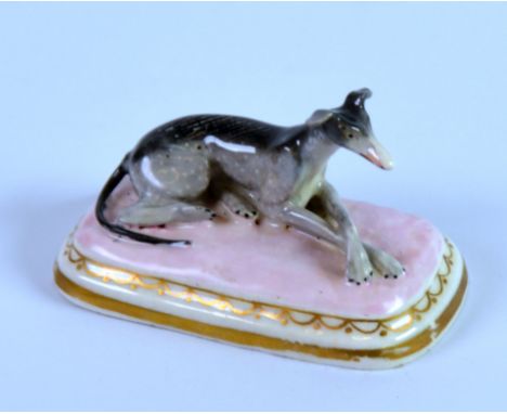 CHAMBERLAIN’S WORCESTER PORCELAIN MODEL OF A RECUMBENT GREYHOUND, painted in colours, on a pink and gilt oblong cushion patte