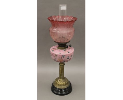 A brass column oil lamp with floral pink font and red etched shade. 66 cm high overall.
