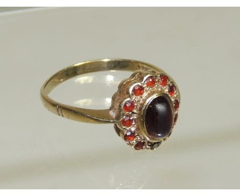 A 9ct gold ladies dress ring set with a central, oval cabouchon garnet with a surround of garnets in an openwork mount.  Ring