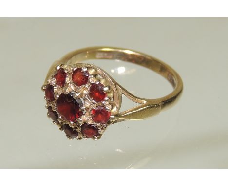 A 9ct gold ladies dress ring set with a central garnet, with a surround of garnets in an openwork mount, ring size N.  