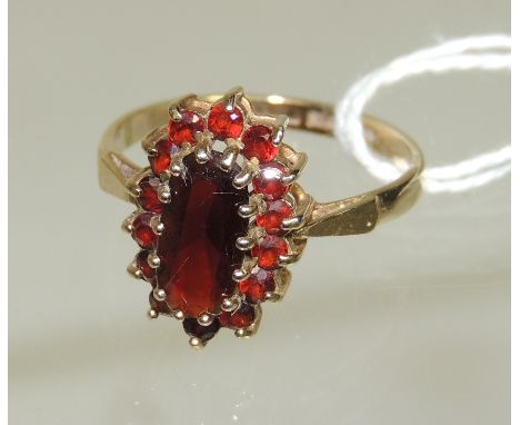 A ladies 9ct gold dress ring set with a central oval garnet with a surround of small garnets in an openwork mount.  Ring size