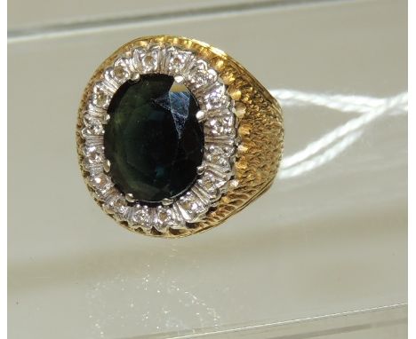 An 18ct gold ladies dress ring, set with a large dark green, oval, faceted topaz with a surround of diamonds in a bark effect