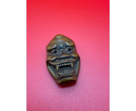 A Japanese hand carved netsuke of an Okimono monster mask, Designed with black bead eyes and signed by the artist. 