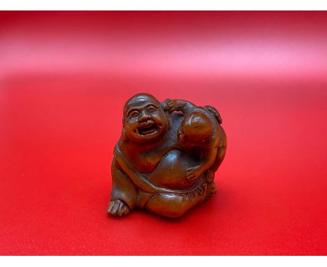 A Japanese hand carved netsuke of a laughing buddha and child. Signed by the artist 