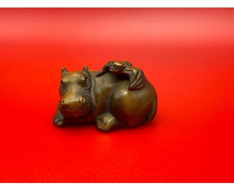 A Japanese hand carved netsuke of a Hippo laying down with a bat on its back. Both have black bead eyes and signed by the art