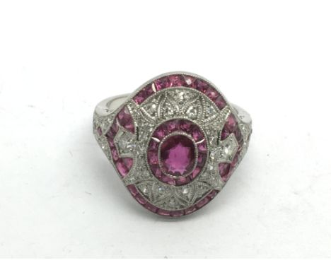 An ornate platinum, ruby and diamond dress ring set with an oval cut ruby surrounded by RBC diamonds and calibre cut rubies, 