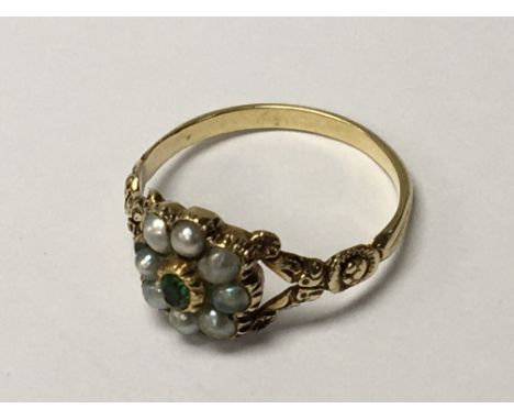 A gold ring unmarked set with a green emerald coloured stone flanked by seed pearls. Ring size K.