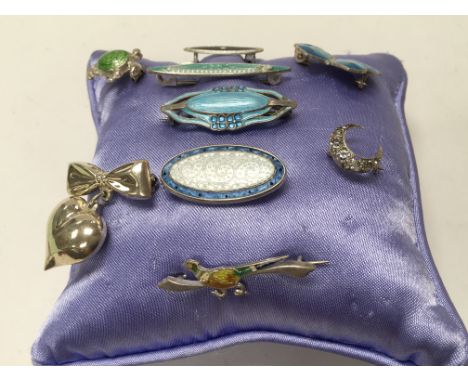 A collection of 9 enamel vintage brooches pinned to a cushion.