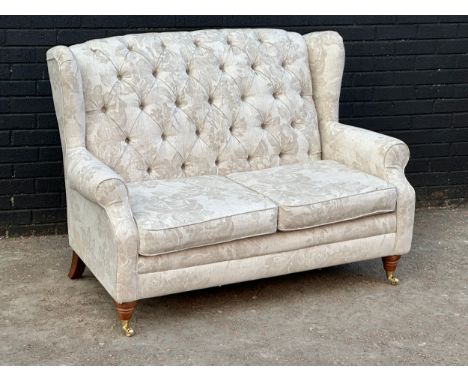 A deep button wingback 2 seater sofa on brass cup casters. 141cm
