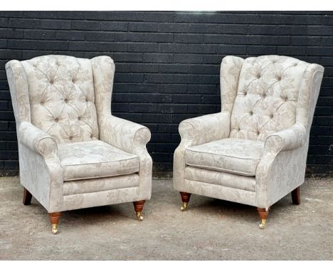 A pair of deep button wingback armchair on brass cup casters. 80x72x101cm