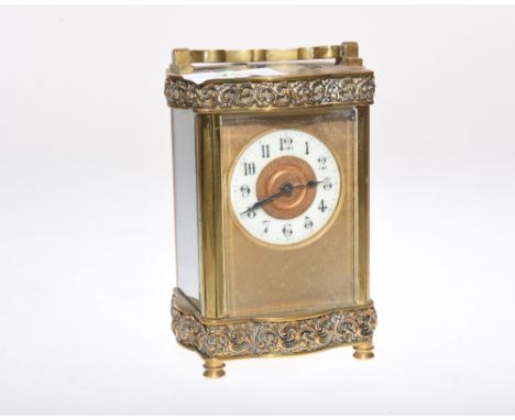 A brass carriage clock with ornate swing handle above a chased border, the white enamel dial with arabic numerals, with key a