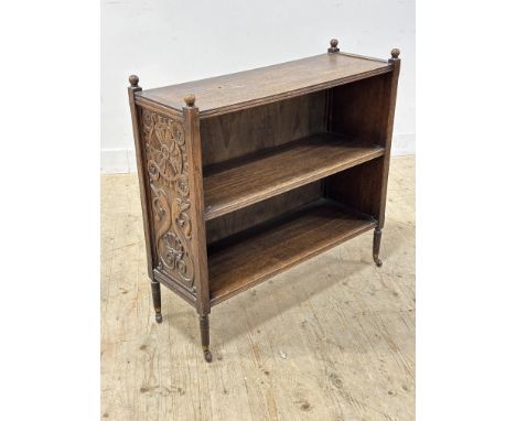 An Edwardian oak Celtic style upright open bookcase fitted two shelves, with relief carved sides, with brass caps and castors