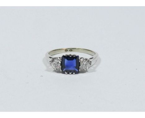Sapphire and diamond cluster ring set with a square sapphire flanked each side by brilliant cut diamonds on a white metal sha