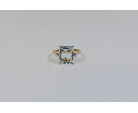 An aquamarine and diamond ring set with a large trap cut aquamarine with small diamonds to the shoulders on an 18ct yellow sh