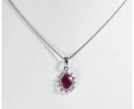 An 18ct white gold ruby and diamond cluster pendant set with a central oval ruby surrounded by 12 brilliant cut diamonds on a