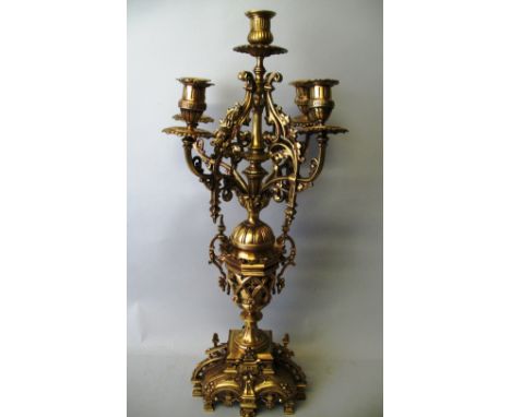 A French ecclesiastical style polished brass five-light candelabra, with ornately pierced scrolling base supporting a two-han