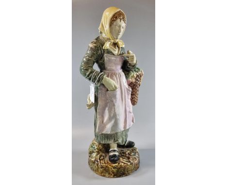 Continental majolica figurine of an old lady in bonnet with basket of flowers, standing on a naturalistic base. 40cm high app