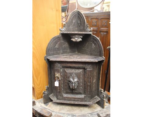 A heavily carved oak corner wall unit, having lion-head decoration to the door, opening to reveal one shelf, brass catch 