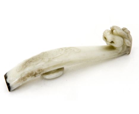 A Chinese carved jade belt hook, modelled as a dragon with relief foliate scroll decoration, the tip highlighted in black, 10