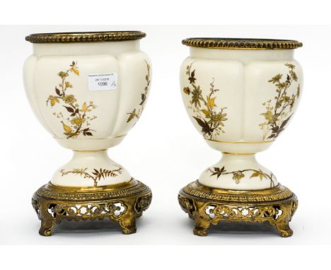 A pair of early 20th Century pedestal urns, probably Royal Worcester, hand gilded with foliage on a cream ground, with a bras