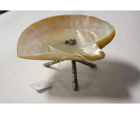 An oyster shell on white metal tripod stand (indistinct hallmarks) having butterfly to the centre 