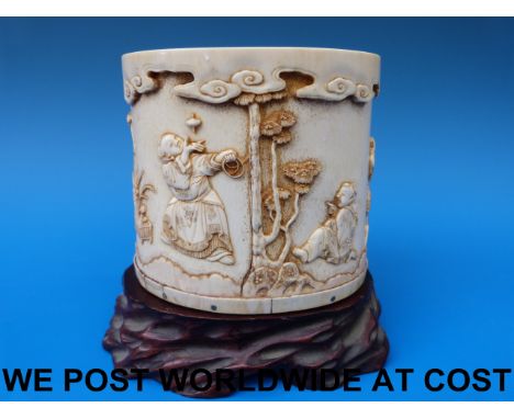 A 19thC Chinese ivory brush pot finely decorated with children and figures playing games, on a naturalistic wooden base