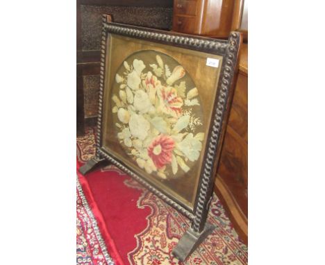An oak raised woolwork and needlepoint firescreen, early 20th century, floral decorated beneath a glazed panel, with a spiral