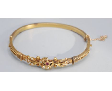 A late Victorian or Edwardian 15ct gold hollow hinged bangle set with half pearl and a ruby, 7.5g.