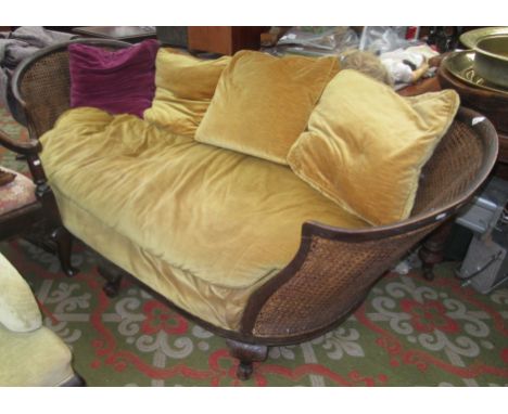 A double caned bergere sofa, 19th century, the shaped wooden rail carved with flowerheads within a cartouche on carved cabrio