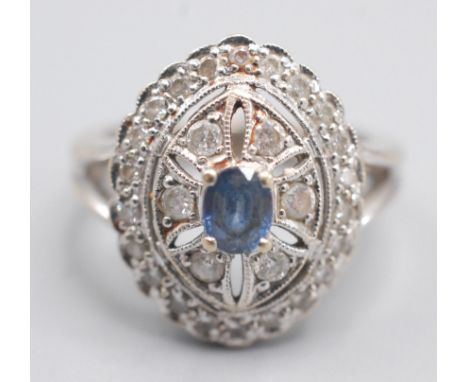 An 18ct white gold eliptical diamond cluster ring with a central oval sapphire.