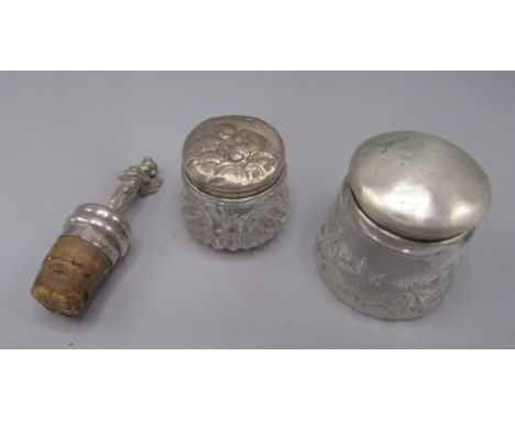 Two glass toilet jars, each with a silver lid, one embossed with winged heads, together with a silver bottle stopper, the fin