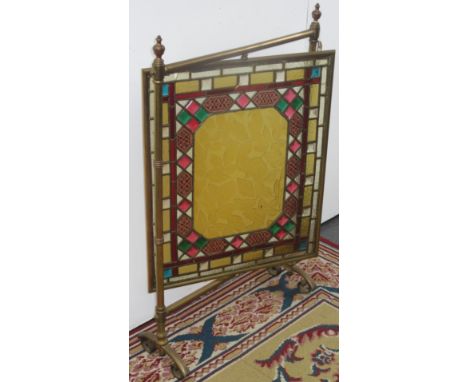 An Arts & Crafts brass firescreen, with a revolving central rectangular stained glass panel decorated with leaves, height 87.