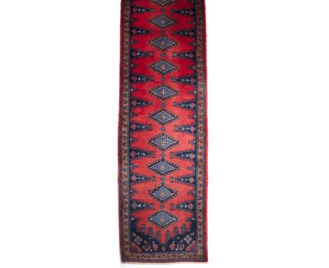 A 20th century Middle Eastern red ground woollen runner with a multiple banded border and geometric decoration, 94cm x 405cmI