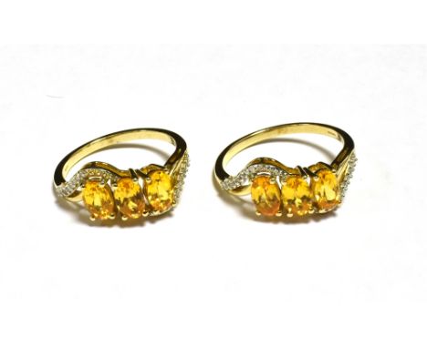 A PAIR OF 9CT GOLD ORANGE GARNET TRIPLE STONE DRESS RINGS Both rings with matched designs featuring white accent cross over s
