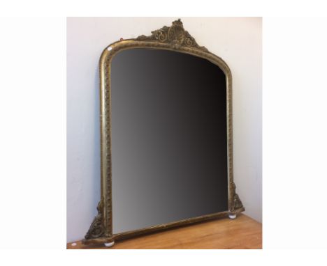 A large 19th Century gilt arch top over mantle mirror, with scrolling corbelles and ceramic feet, surmounted with scrolls and
