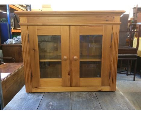 A contemporary pine wall mounted cupboard, having two glazed doors with a single adjustable shelf to the inside, 80cm x 30cm 