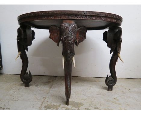 An early 20th century Indian carved hardwood occasional table, the oval top decorated with figures, elephants and flora on el