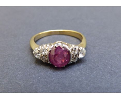 A ruby and diamond set yellow metal ring, the oval ruby flanked by six small old cut diamonds.  Finger size P.
