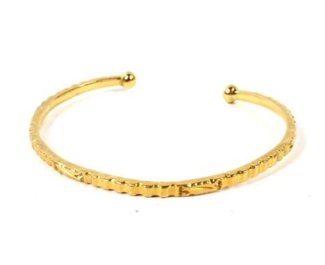 An Indian high carat textured and carved yellow metal torque bangle. With bead terminals, unmarked, 21.1g Condition Report: T