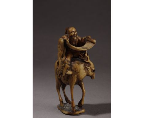 A mid 19th century Japanese netsuke from Edo period. In carved elephant ivory portraying a philosopher with horn eyes, riding