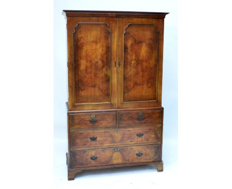 An early 20th century walnut linen press, the moulded cornice above two cupboard doors enclosing two later shelves above a ba
