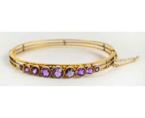 A yellow metal and amethyst hinged bangle, the open framework set with nine graduated circular cut amethysts complete with sa