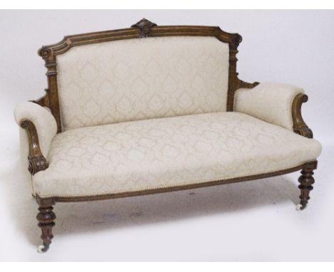 A Victorian carved walnut framed sofa with architectural back, outswept arms, and turned carved supports to castors, upholste