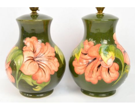 A pair of Moorcroft lamp bases in pink hibiscus pattern on a green ground, one stamped Moorcroft to base, the other with a pa