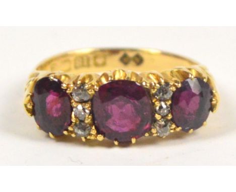 An 18ct yellow gold dress ring set with three rubies, the central stone 0.75ct, and six diamond chips with engraving to the s