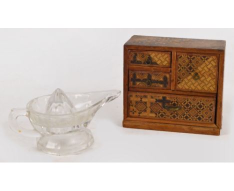 A vintage pressed clear glass lemon squeezer in the form of an oil lamp and a miniature marquetry inlaid chest of four drawer