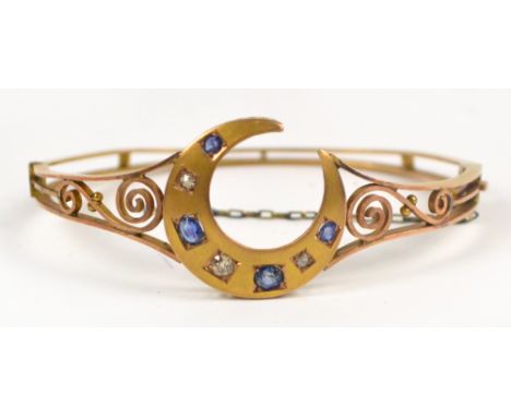 An Edwardian yellow metal snap bangle with filigree scroll decoration centred by a crescent on pierced gallery, set with four