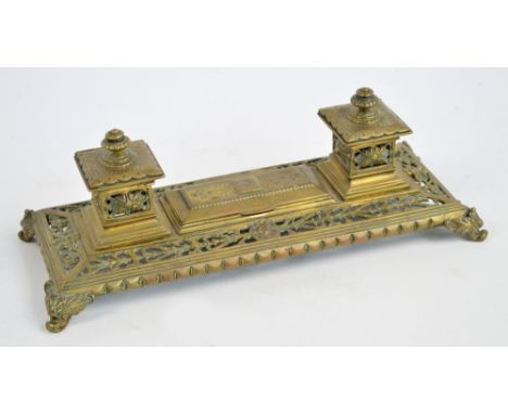A late 19th century brass rectangular ink stand pierced with foliate scrolls, with two ink wells with ceramic liners flanking